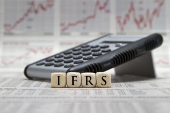 Taschenrechner, im Vordergrund stehen Holzwürfel auf denen IFRS steht