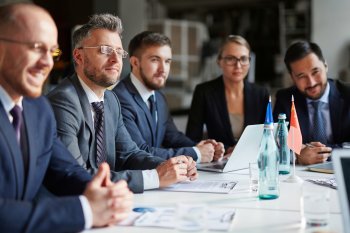 Personen in Anzügen sitzen um einen Tisch im Business-Meeting