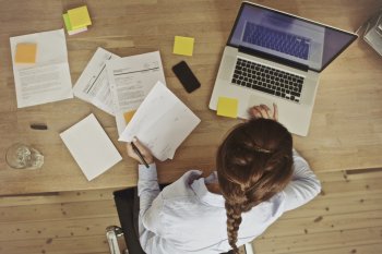Auslandsstudium Studienleistungen checken Sicht von oben auf Studentin, die mit Laptop und Unterlagen am Tisch sitzt