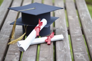 Zwei Doktorhüte übereinander gestapelt und zwei Abschlussurkunden zusammengerollt