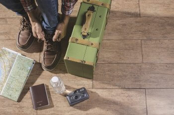 Junger Mann bindet sich Schuhe zu, neben ihm steht ein Koffer und Reiseutensilien