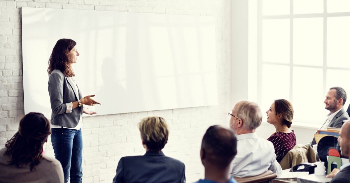 Weiterbildungen in der Übersicht Dozentin steht vorne an Whiteboard, um sie herum sitzen ältere Studenten