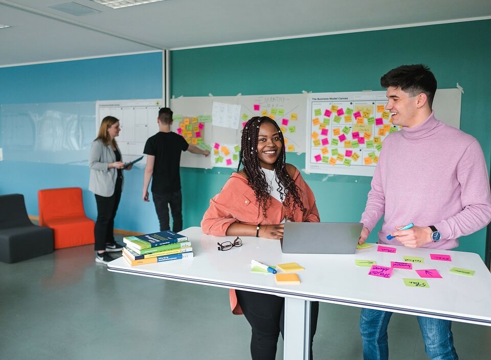 Studierende der Hochschule Stralsund stehen an einem Tisch und bereiten Zettel für das Brainstorming an der Tafel im Hintergrund